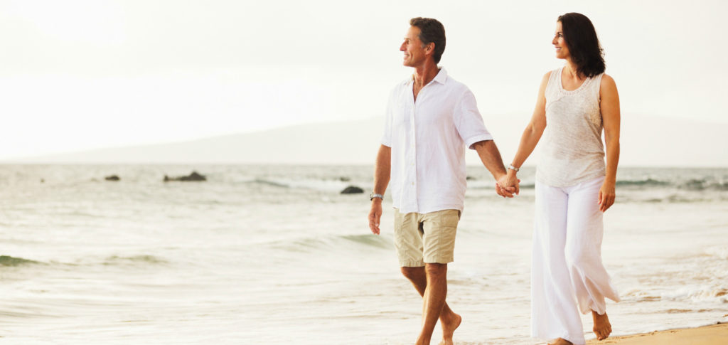 Photo of a man and woman walking on a beach, looking peaceful.